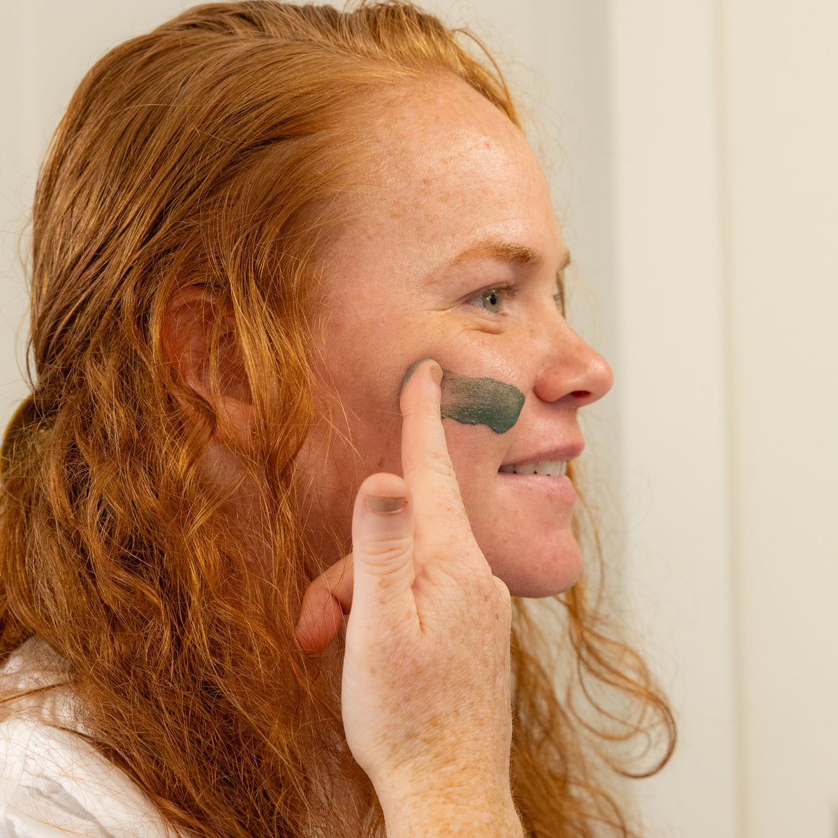 Woman applying green mask to her cheek.