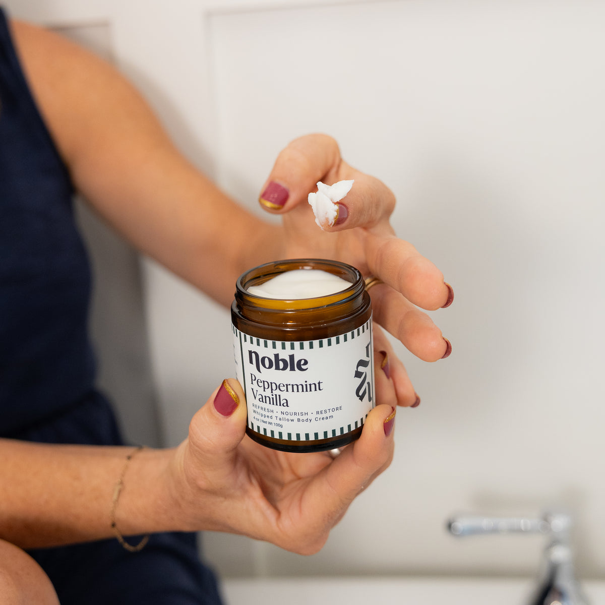 Person holding an open Peppermint Vanilla Body Tallow jar with cream on a finger.