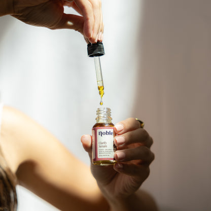 Glass dropper above an open Clarify Face Serum bottle.