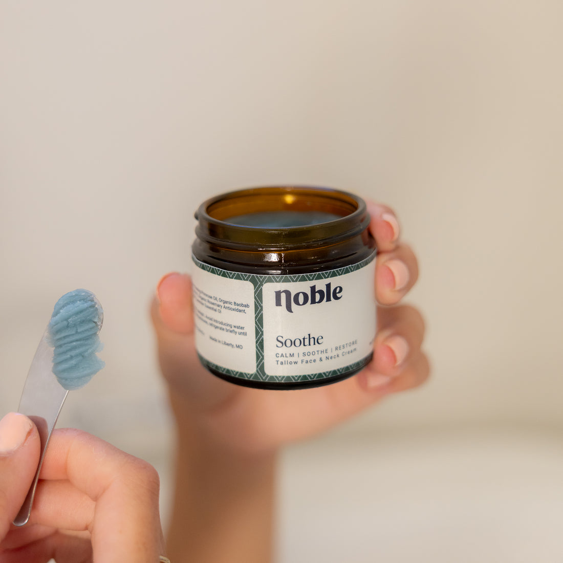 Hand holding a Soothe Face Cream jar beside blue-green cream on a spatula.