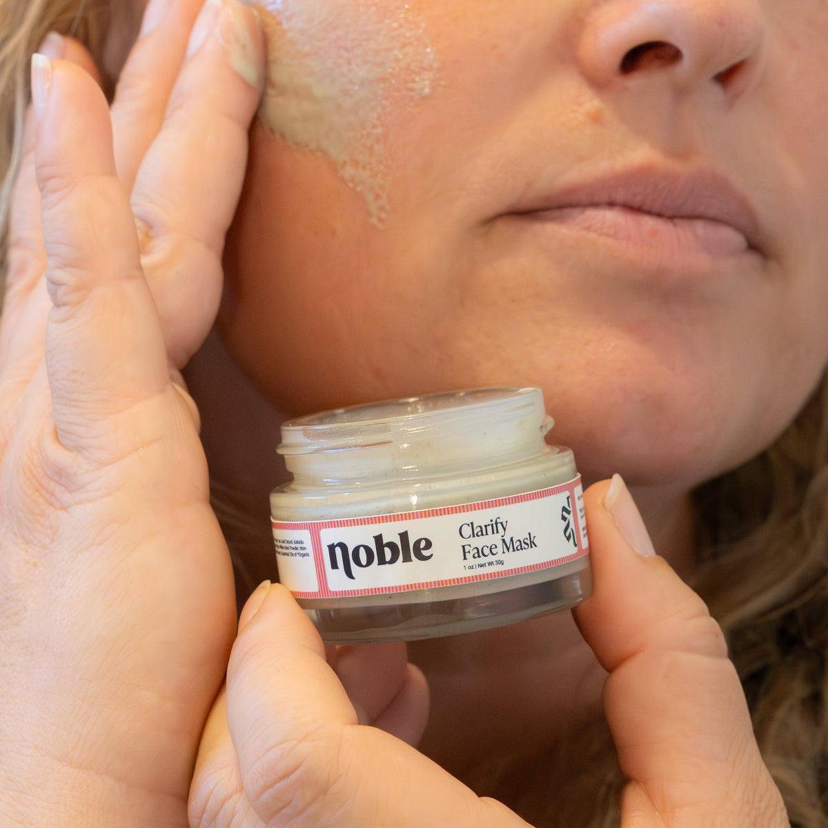 Woman applying Clarify Face Mask while holding the open jar.