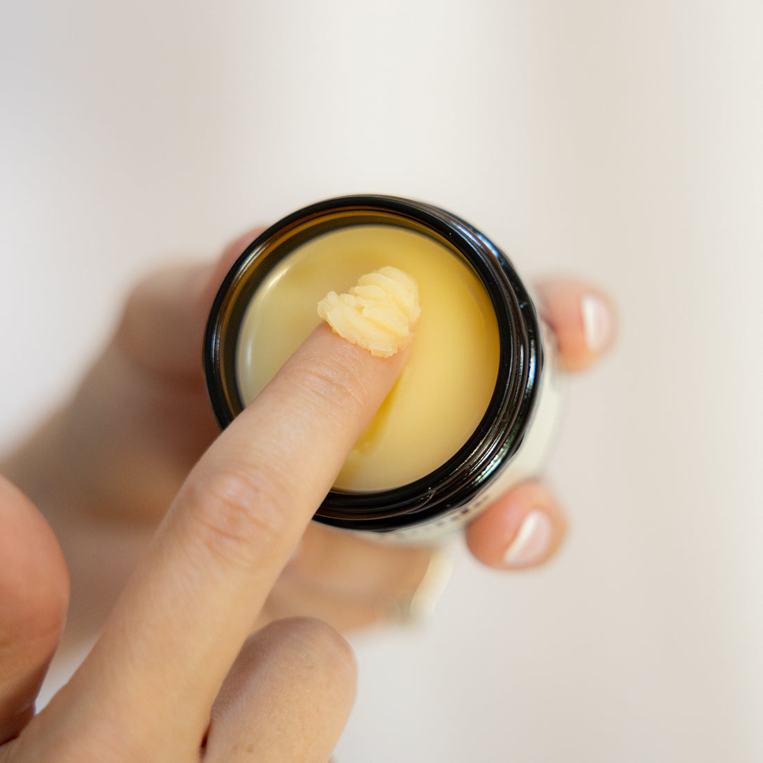 Finger scooping golden cream from an open jar.