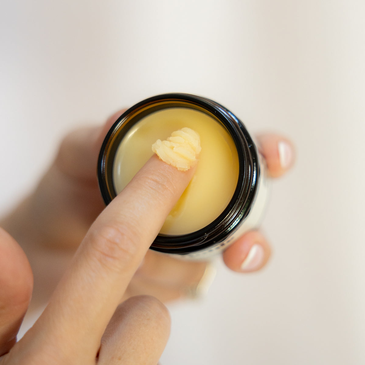 Finger scooping golden cream from an open jar.