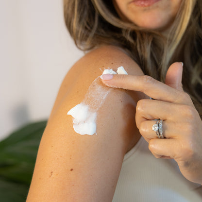 Finger spreading white cream over a shoulder.