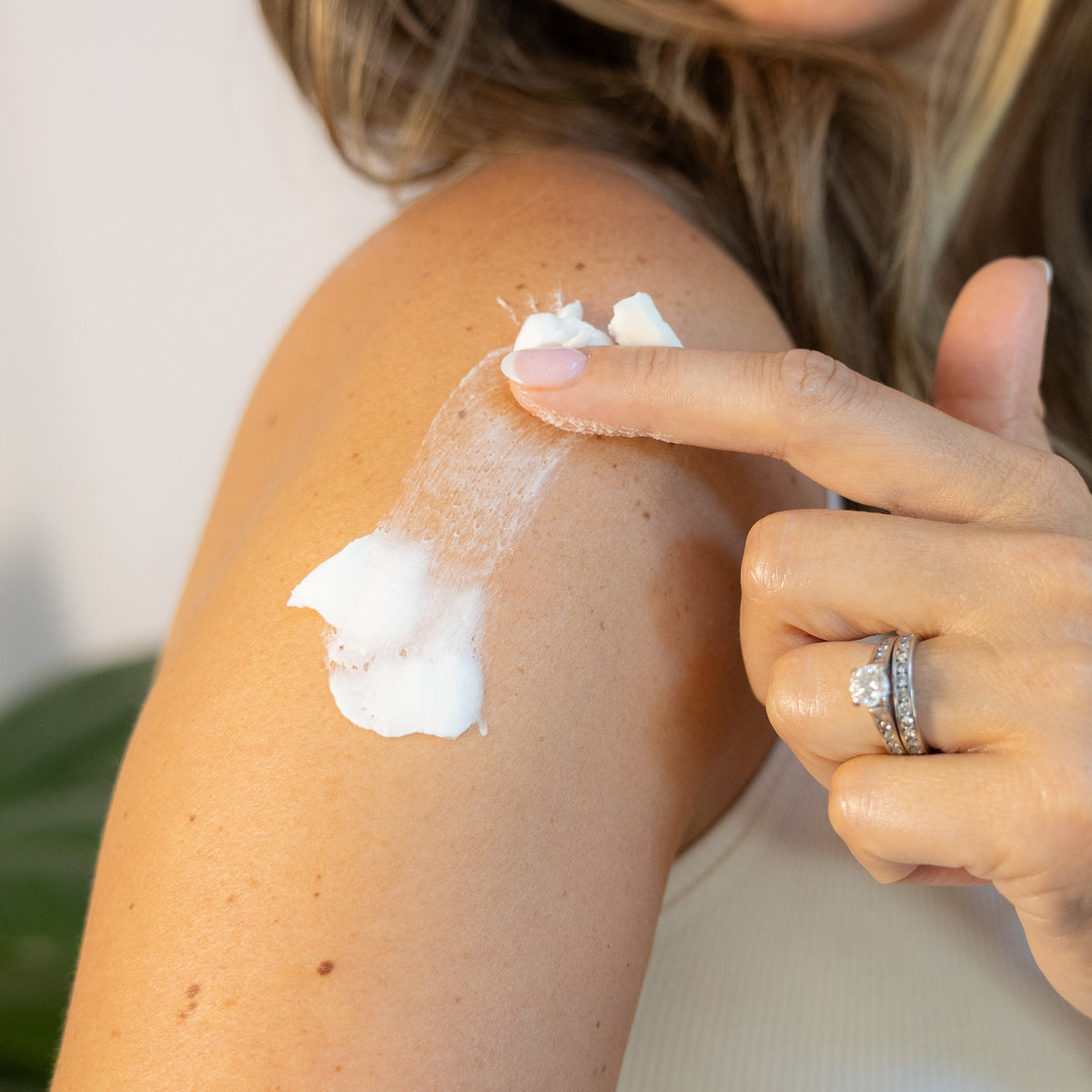 Finger spreading white cream over a shoulder.
