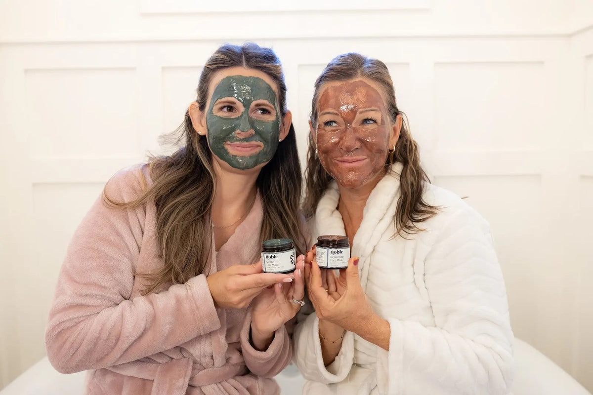 Two women holding Noble Soothe Face Mask and Rejuvenate Face Mask while wearing the masks.