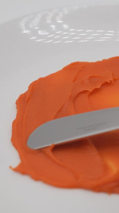 Antioxidant Repair Balm’s orange-red texture spread with a cosmetic spatula.