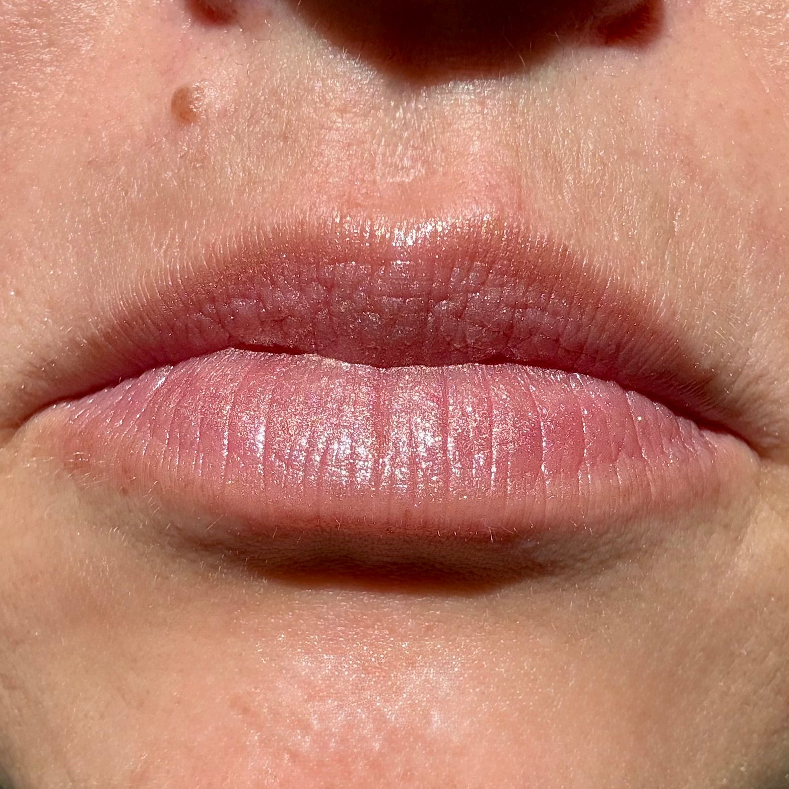 Close-up of lips wearing Sun-Kissed tinted lip balm by Noble Skin Co., a warm bronzed pink shade with a soft golden glow and dewy finish